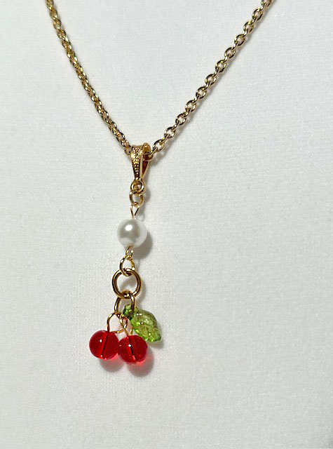 Gold necklace with a pendant featuring cherries and leaf.